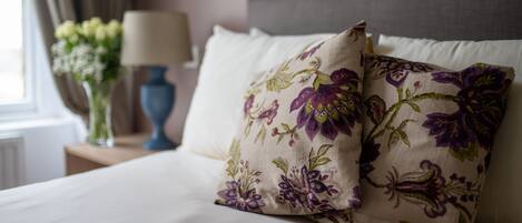 A neatly made bed with floral pillows, a bedside lamp, and a vase with flowers on a nightstand.