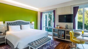 A hotel room with a bed, a desk with a chair, a television, and a window with curtains.