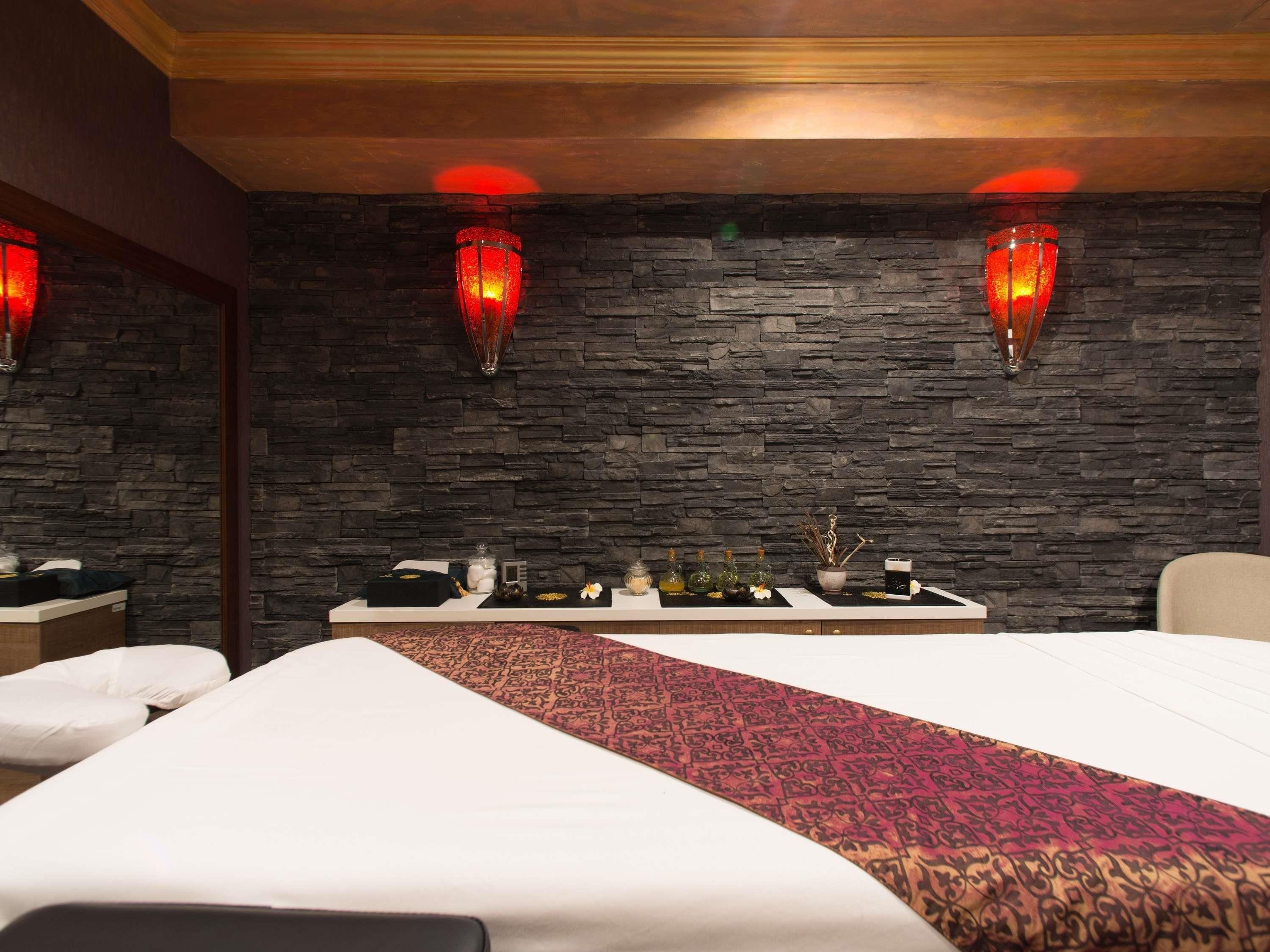 Un cuarto de spa con dos camas, una mesa de masaje, un mostrador de recepción y decoración de pared de piedra.