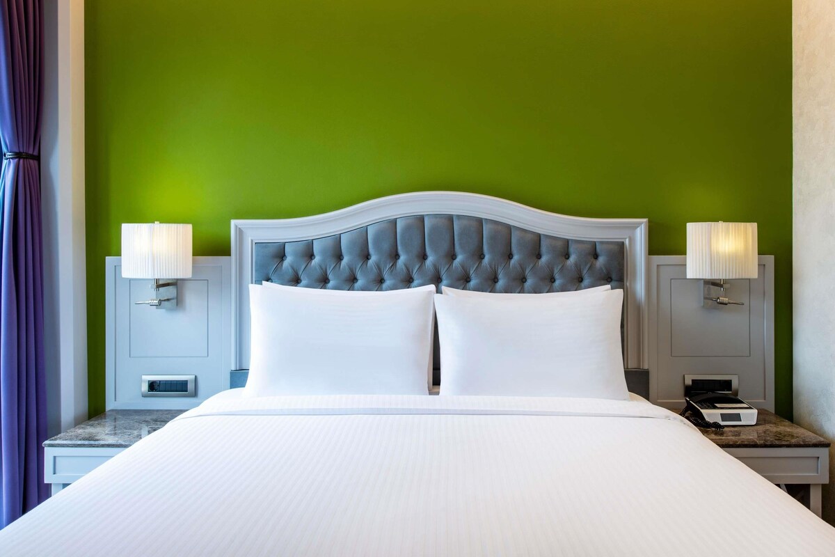 Una habitación de hotel con una cama grande, dos mesitas de noche y una pared verde.