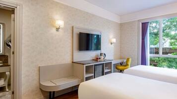 Habitación de hotel con cama, escritorio con silla, televisor y ventana con cortinas.