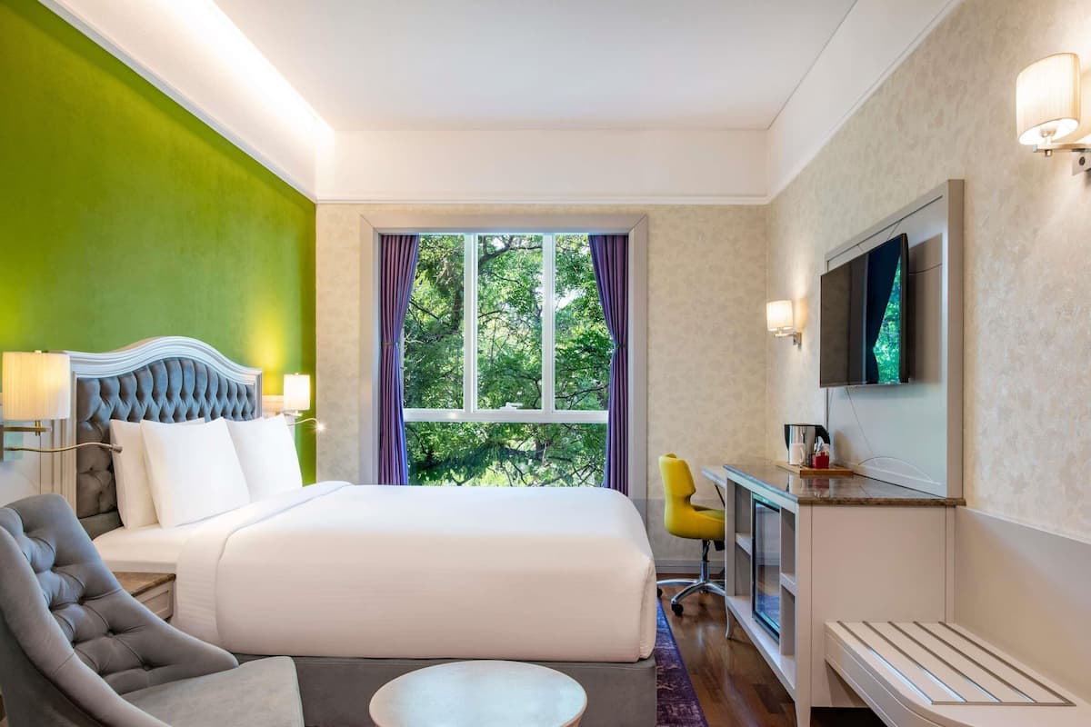 Une chambre d’hôtel avec un lit, une chaise, un bureau, une télévision et une fenêtre avec des rideaux.