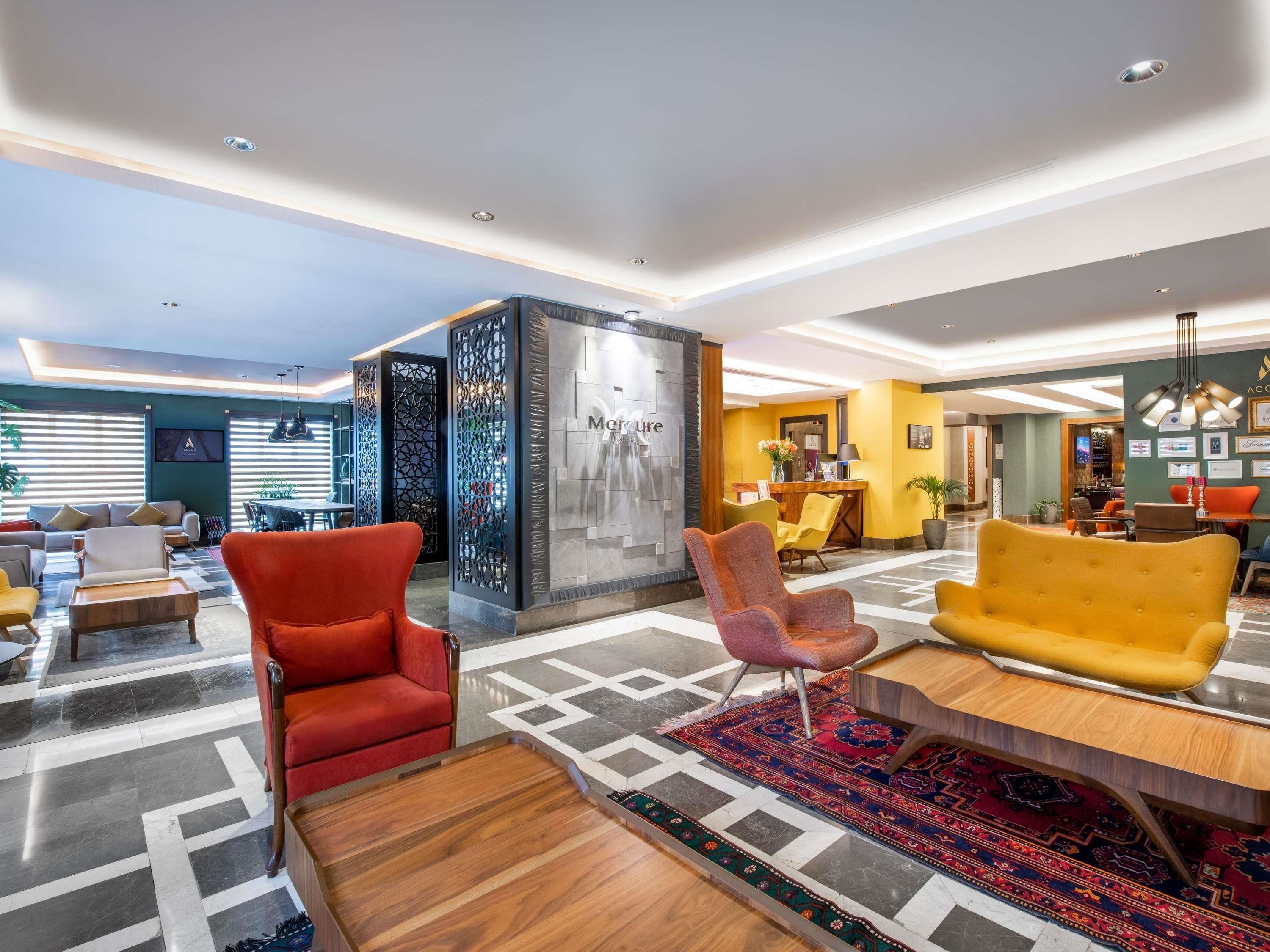 Een moderne lobby met een receptiebalie, zithoeken en een decoratieve muur met een 'Mercure' bord.