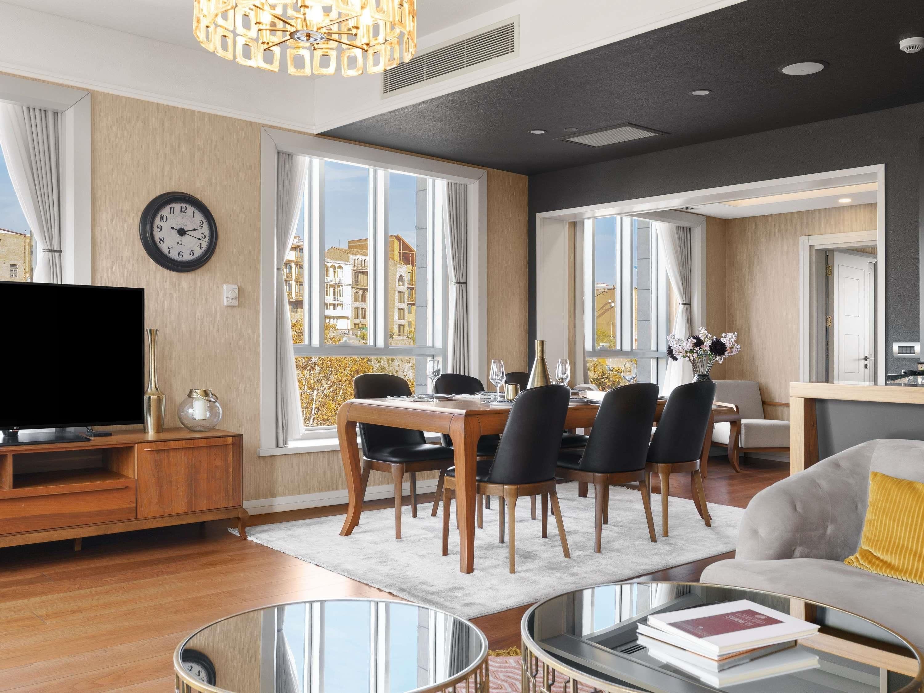 A modern living room with a flat-screen TV, dining area with chairs, a sofa, and a coffee table.