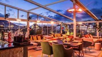 Eine Dachterrasse mit Sitzgelegenheiten, eine Bar mit Flaschen und Blick auf die Stadt.