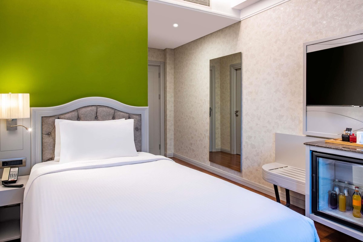 Una habitación de hotel con cama, televisión, minibar y puerta al baño.