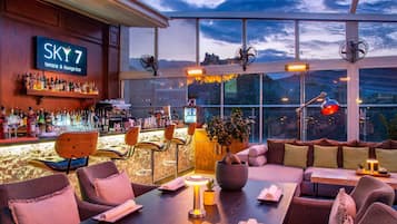 A bar area with a sign reading 'SKY 7 terrace & lounge bar,' bar stools, a bar counter with bottles, and a seating area with tables and chairs.