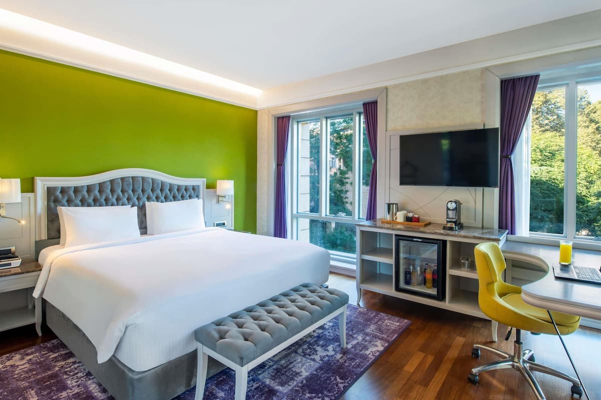 Ein Hotelzimmer mit Bett, Schreibtisch mit Stuhl, Fernseher und einem fensterbepflanzten Fenster.