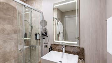 A modern bathroom with a glass-enclosed shower, a standalone sink, and a mirror with integrated lighting.