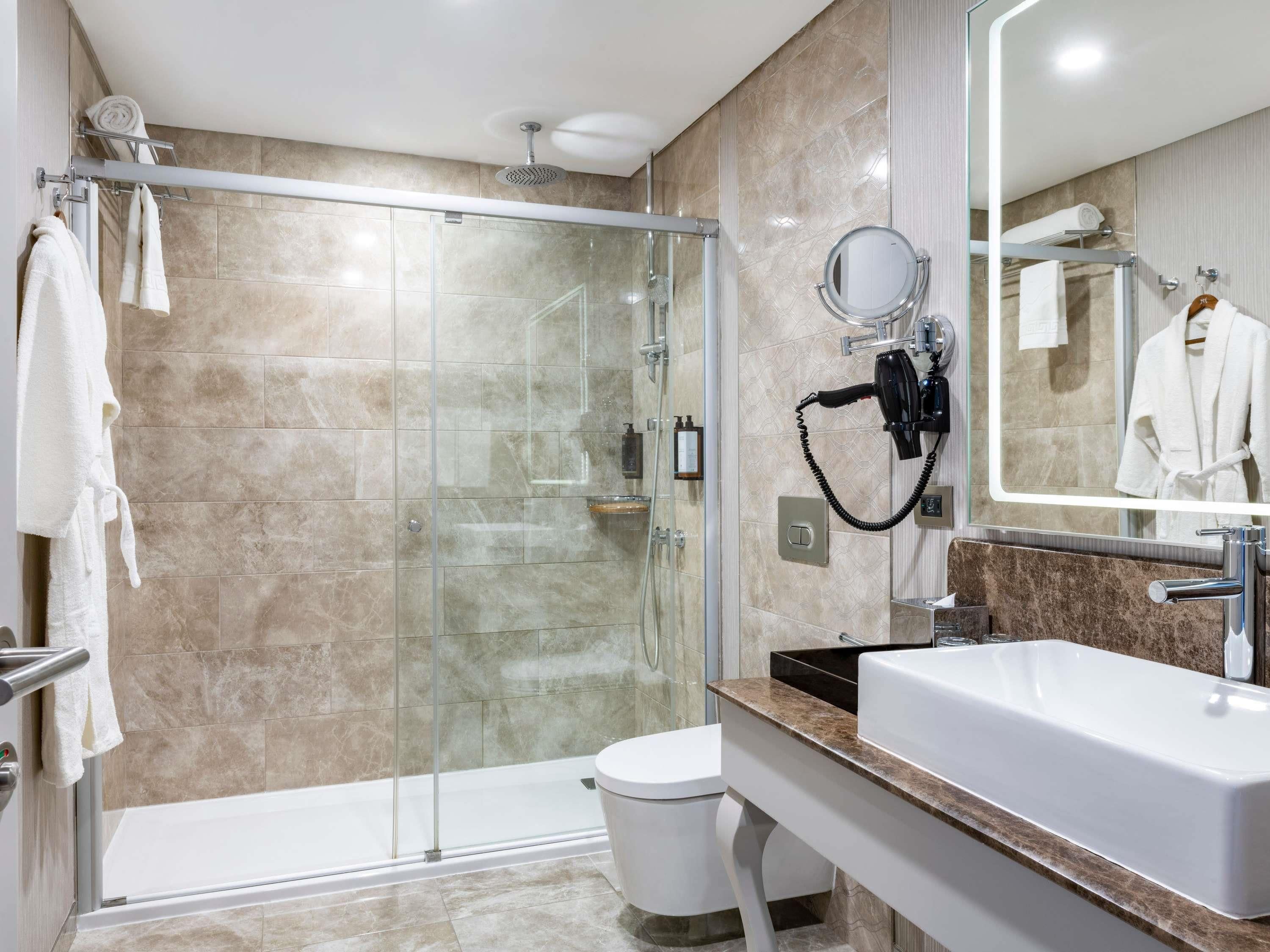 A modern bathroom with a glass shower enclosure, a white toilet, a sink with a marble countertop, and a mirror with a towel rack.