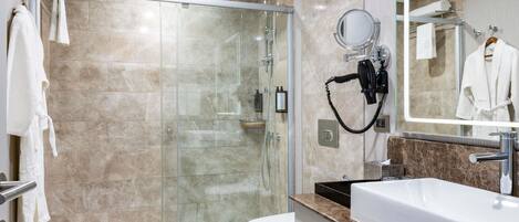 A modern bathroom with a glass shower enclosure, a white toilet, a sink with a marble countertop, and a mirror with a towel rack.