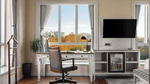 A modern living room with a large window, a flat-screen TV, a desk with a chair, and a sofa.