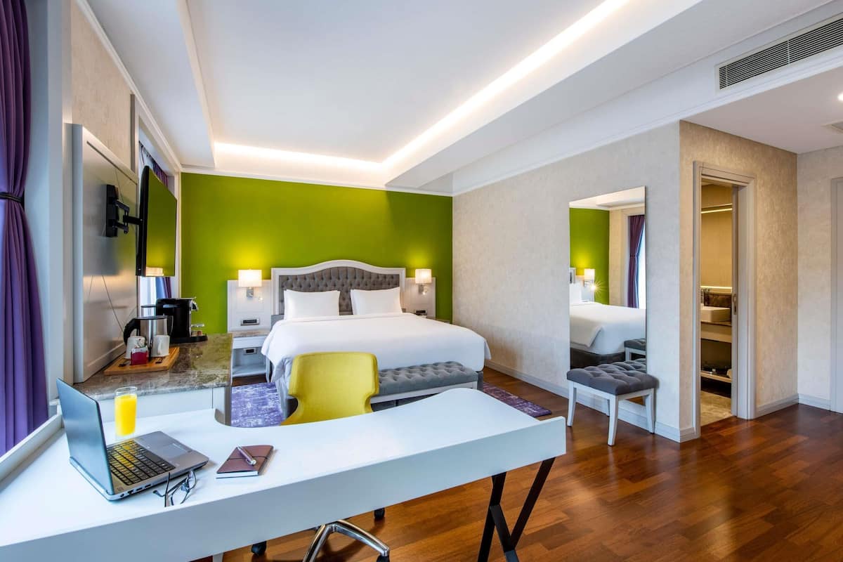 Une chambre d’hôtel moderne avec un grand lit, un bureau avec un ordinateur portable, une chaise et une petite table.