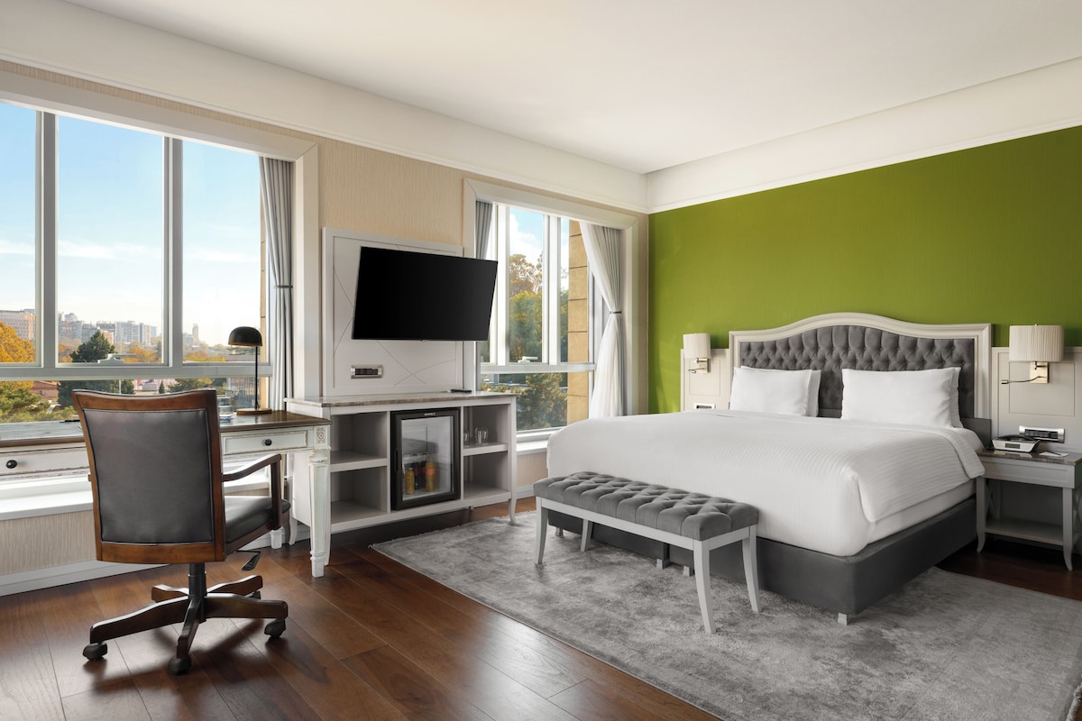 Una habitación de hotel moderna con una cama grande, un escritorio con televisor de pantalla plana, una silla y un banco.
