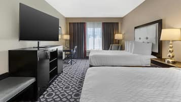 A hotel room with two beds, a desk with a chair, a flat-screen TV, and a large window with curtains.