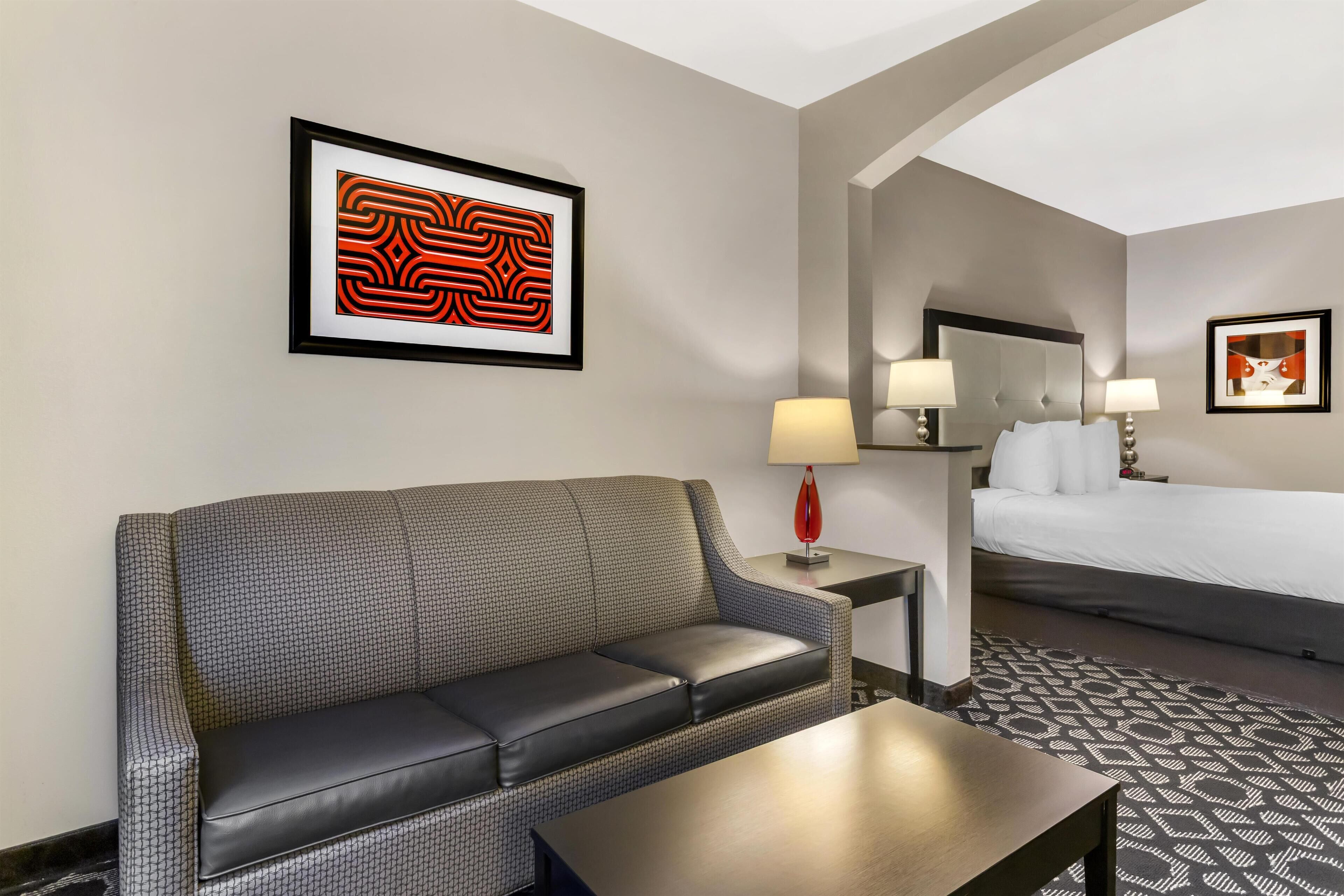 A hotel room with a sofa, a small table, a bed, and a nightstand with a lamp.
