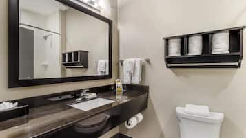 A modern bathroom with a large mirror, a sink, a toilet, and a shelf with towels.
