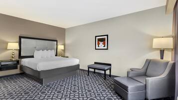 A hotel room with a large bed, a chair, a small table, and a wall-mounted artwork.