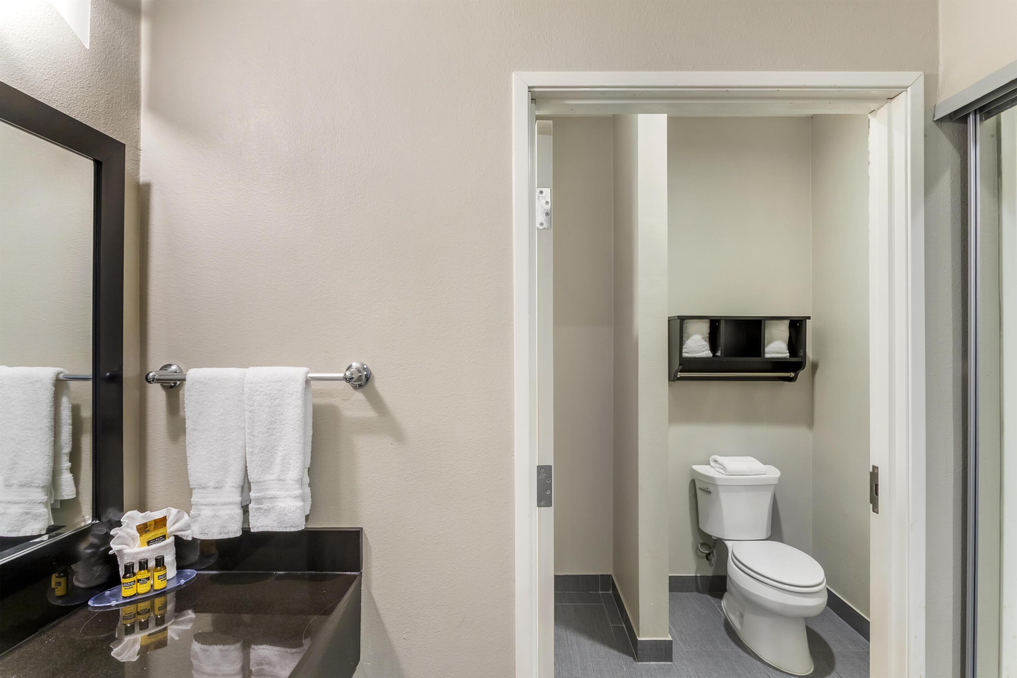 A bathroom with a black sink, white towels, a mirror, and a toilet.