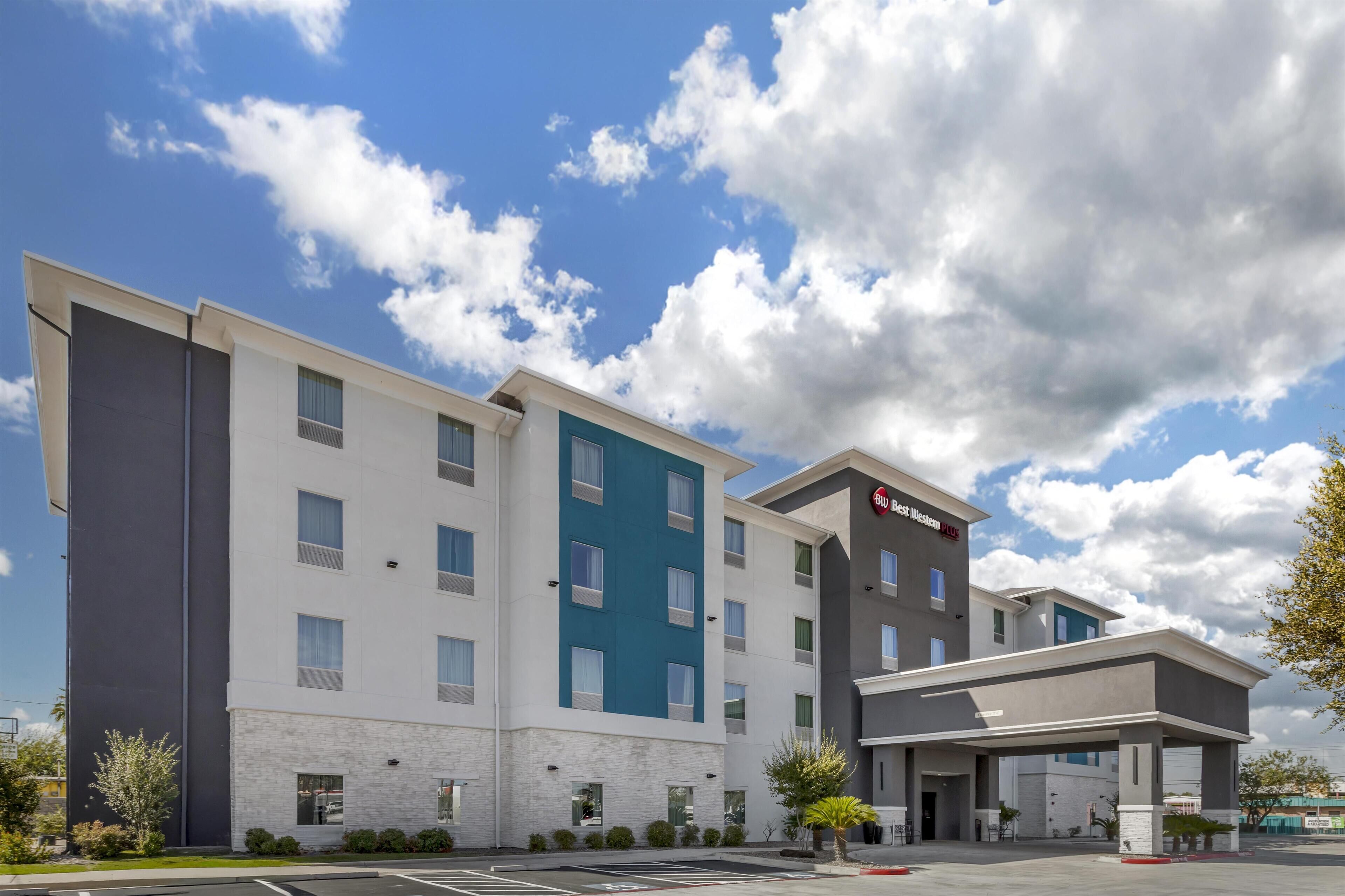 Ein mehrstöckiges Hotel mit modernem Design, mit einer Fassade in Weiß- und Blautönen sowie einem Parkplatz davor.