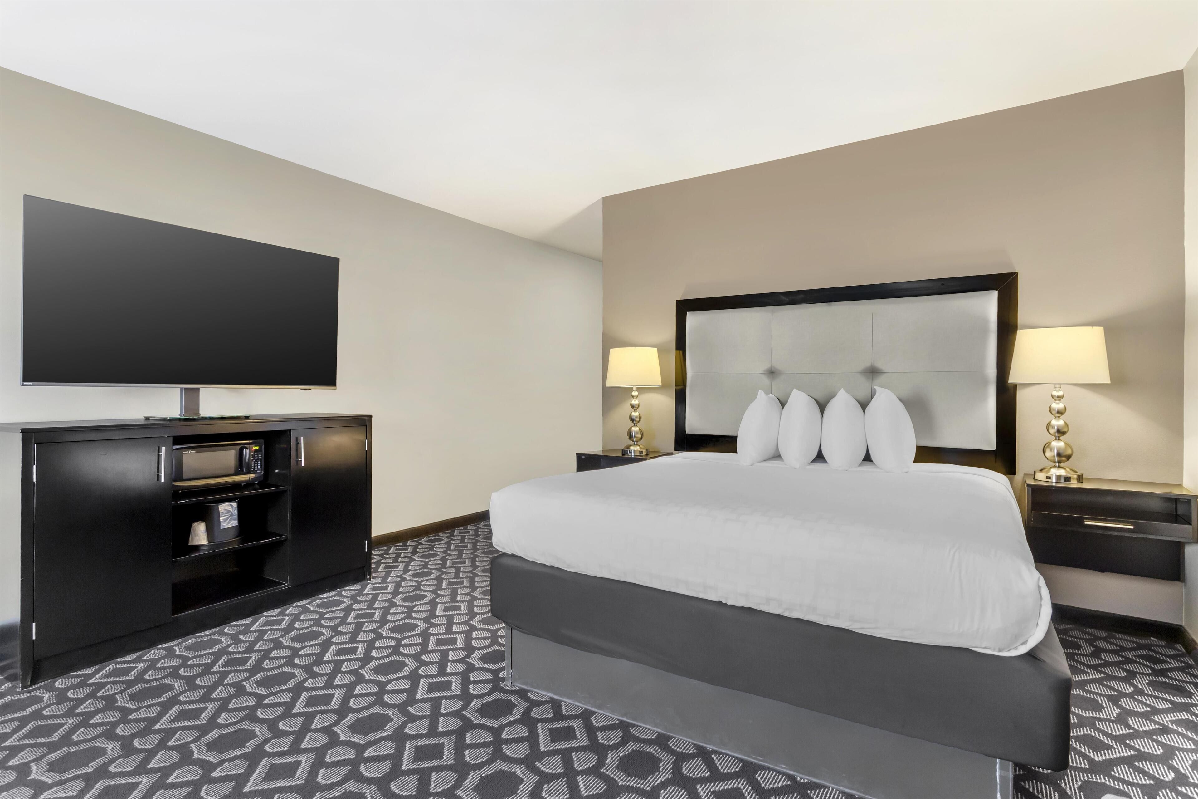 A hotel room with a large bed, a flat-screen TV, a minibar, and two bedside lamps.