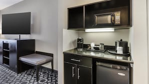 A compact hotel room with a flat-screen TV, a kitchenette with a microwave, coffee maker, and refrigerator, a small seating area with a bench, and a patterned floor. - Best Western Plus Laredo Inn & Suites (Laredo)