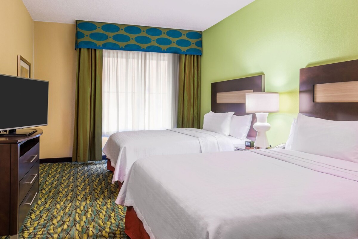 Habitación de hotel con dos camas, televisión, escritorio y ventana con cortinas.