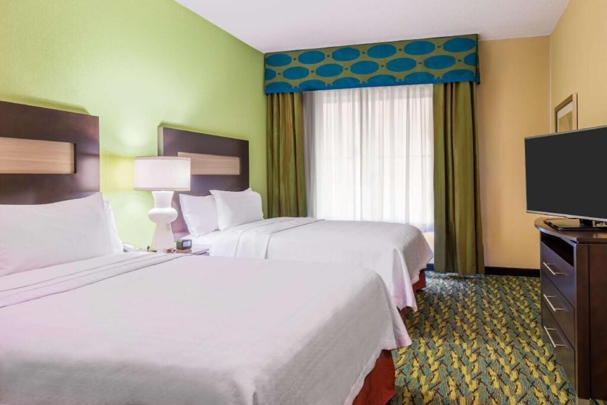 Habitación de hotel con dos camas, televisión, escritorio y alfombra estampada.