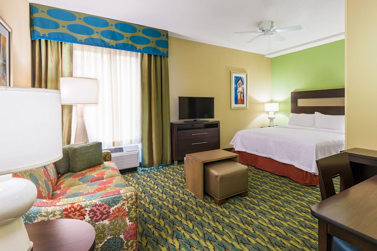 A hotel room with a bed, a sofa, a television, a desk, and a ceiling fan.