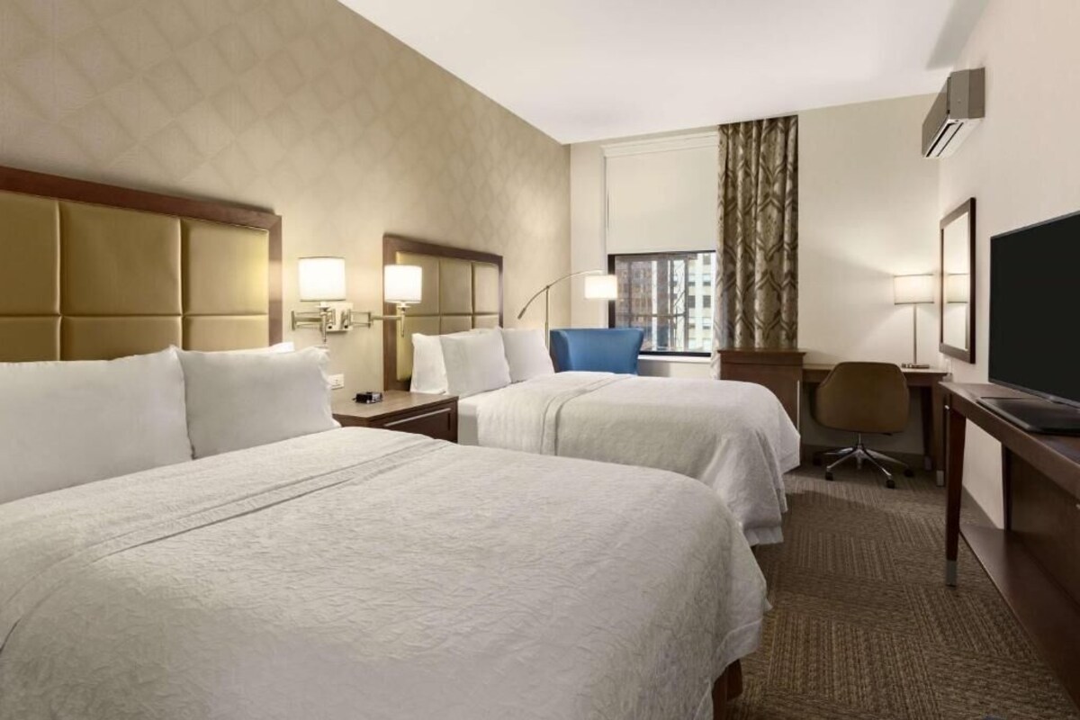 Une chambre d’hôtel avec deux lits, un bureau, une chaise, une télévision et une fenêtre avec des rideaux.