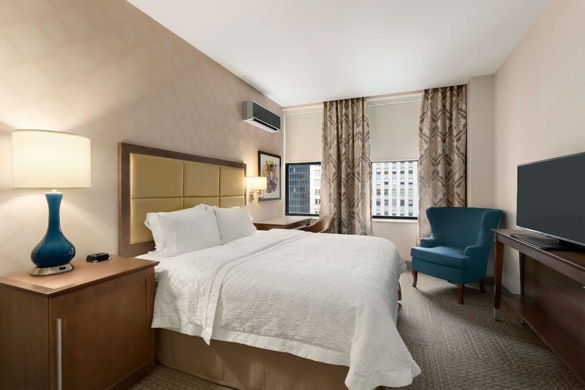 A hotel room with a bed, a desk, a chair, a TV, and a window with curtains.