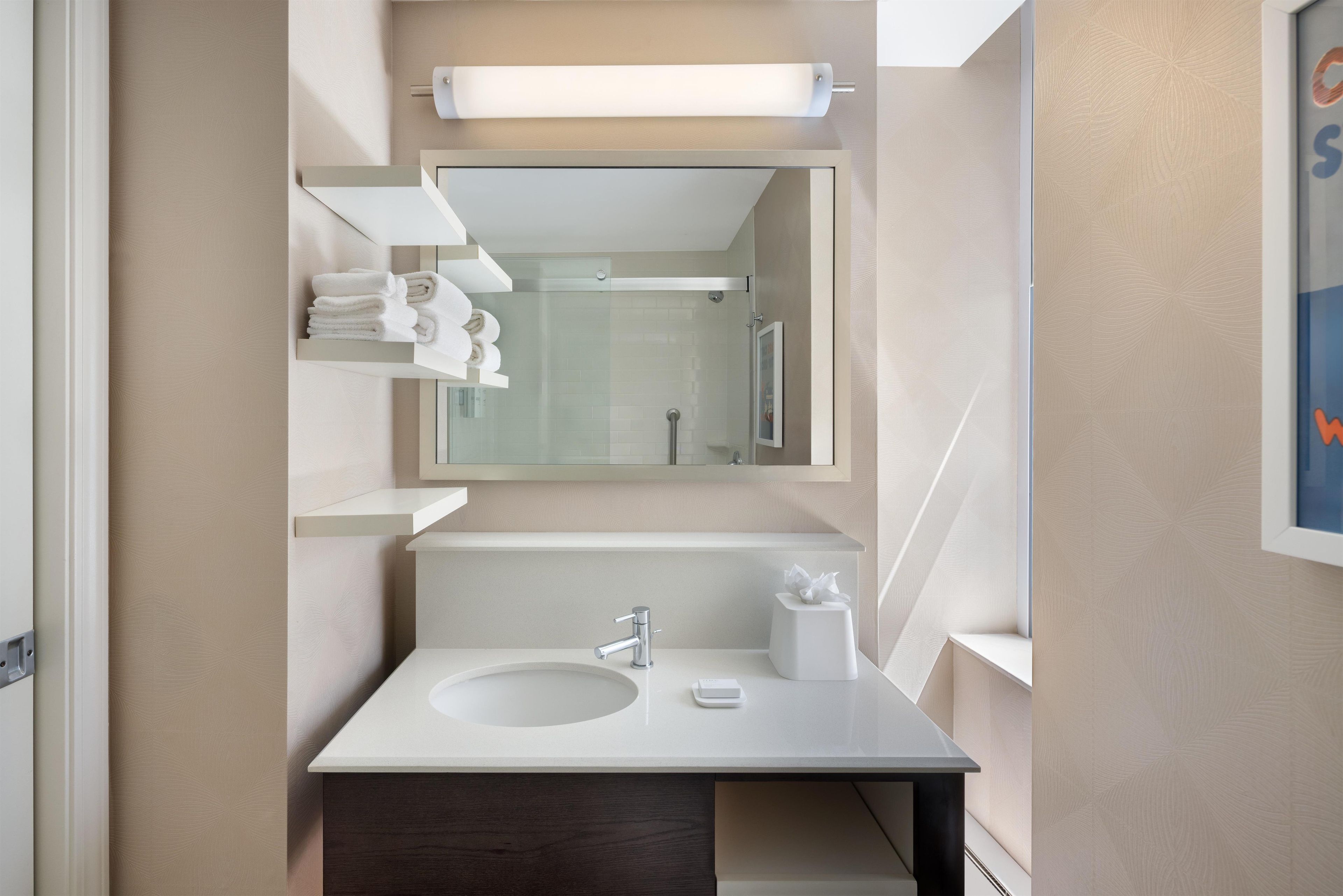 A modern bathroom with a large mirror, a sink, and a towel rack.
