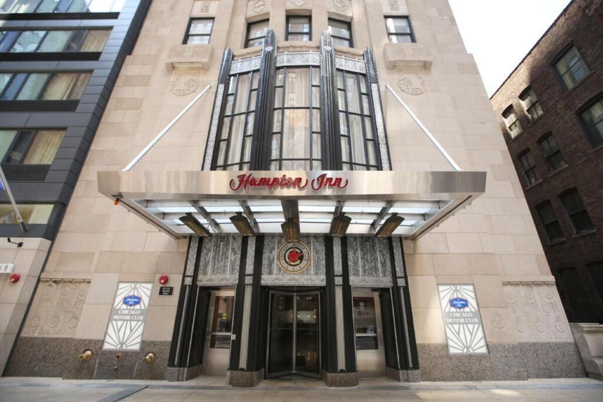 L’entrée d’un hôtel, avec un auvent décoratif, une grande porte vitrée et un panneau indiquant qu’il s’agit d’un club automobile.
