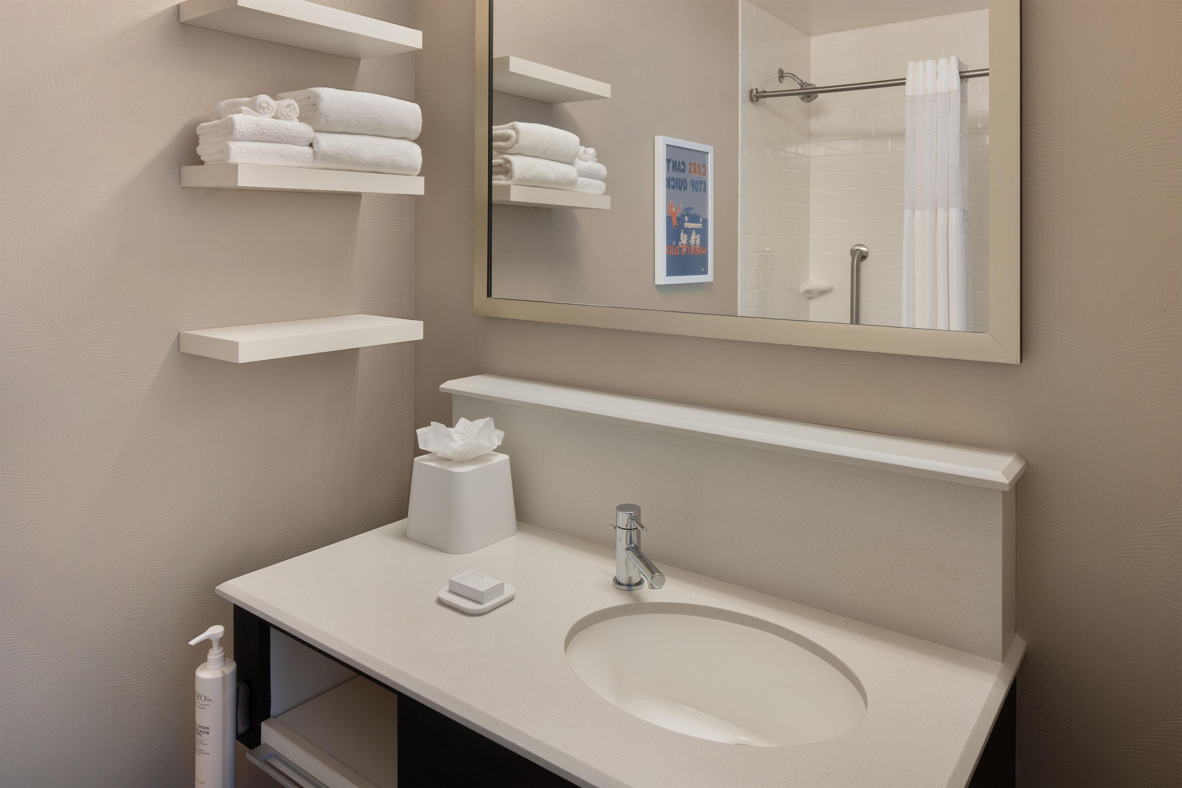 A bathroom with a white sink, a mirror, and shelves with folded towels.