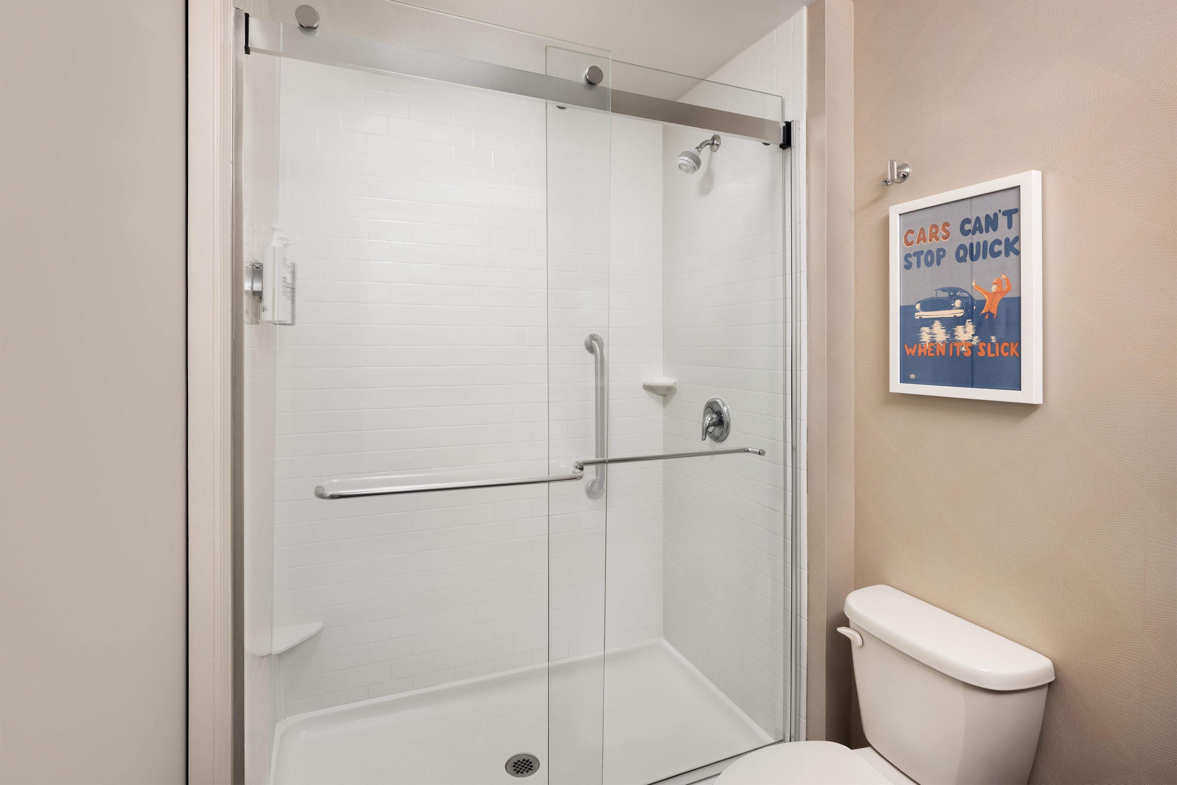 A bathroom with a glass-enclosed shower, a toilet, and a poster on the wall.