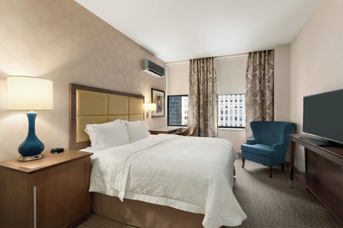 Une chambre d’hôtel avec un lit, un bureau avec une lampe, une télévision et une chaise.