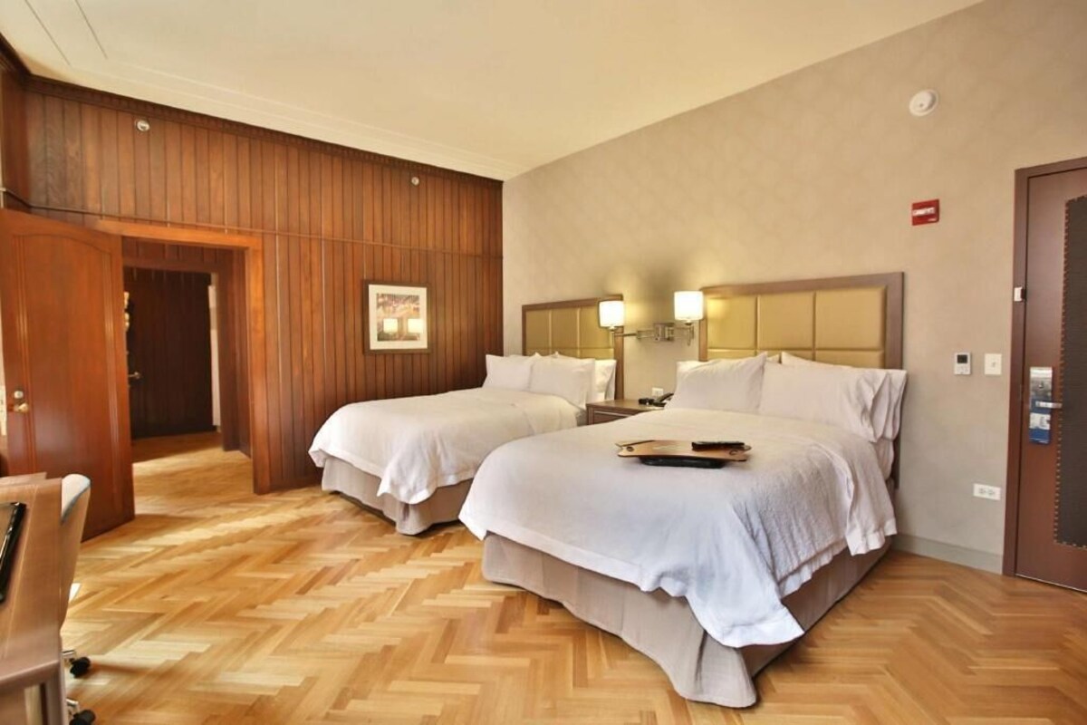 Une chambre d’hôtel avec deux lits, des lambris en bois, un plancher en bois, un bureau et une chaise.