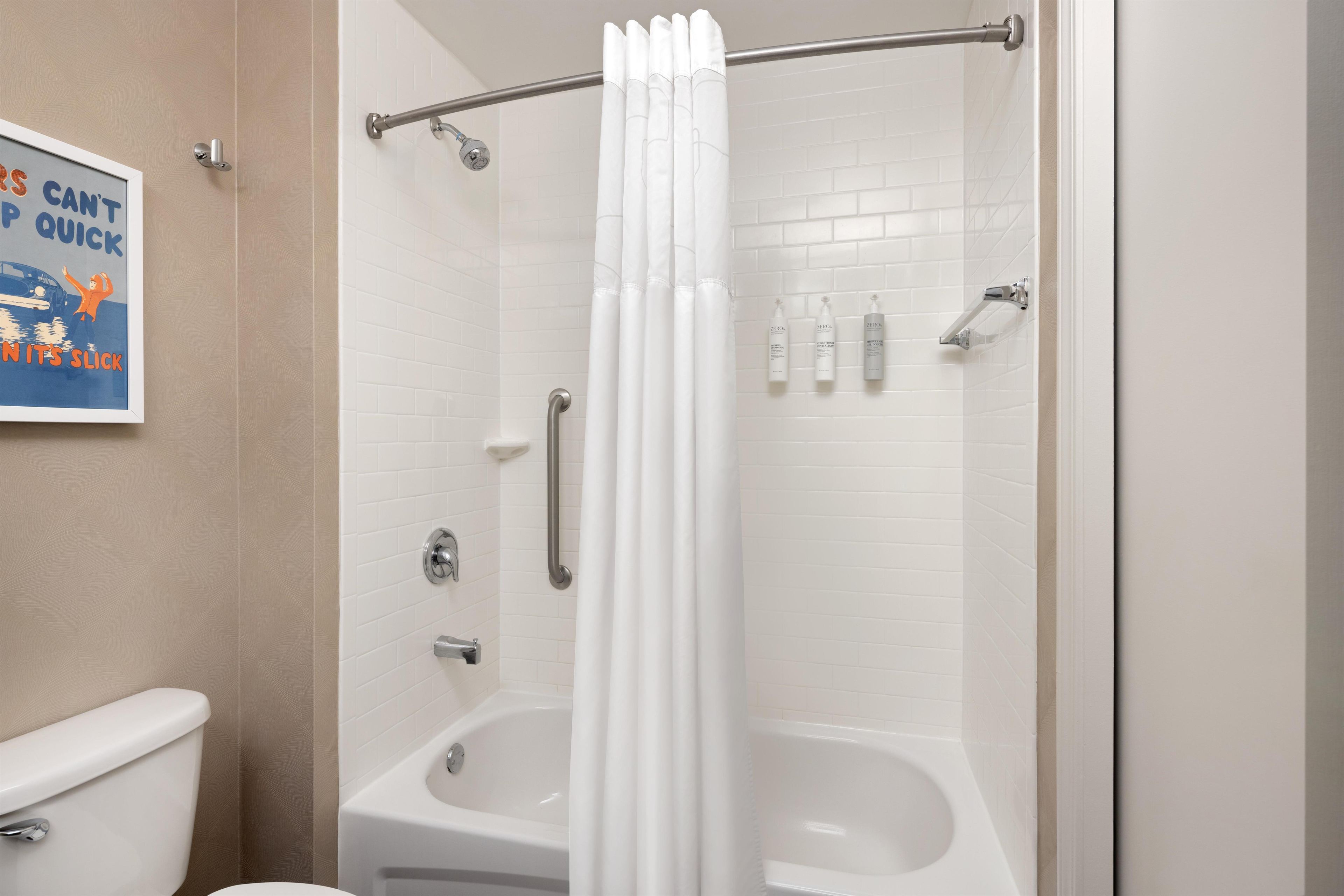 A bathroom with a shower, toilet, and a framed poster on the wall.