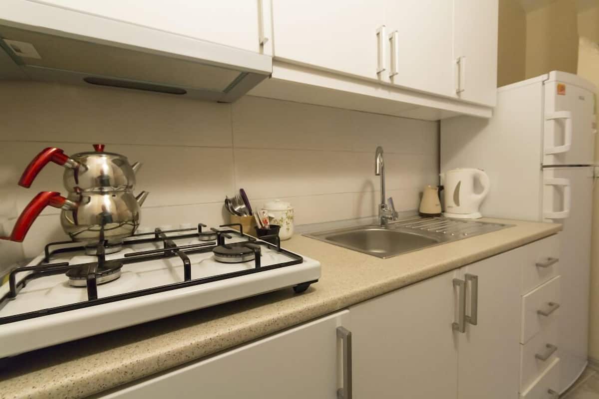 A kitchen with white cabinets, a gas stove, a kettle, a sink, and a refrigerator.