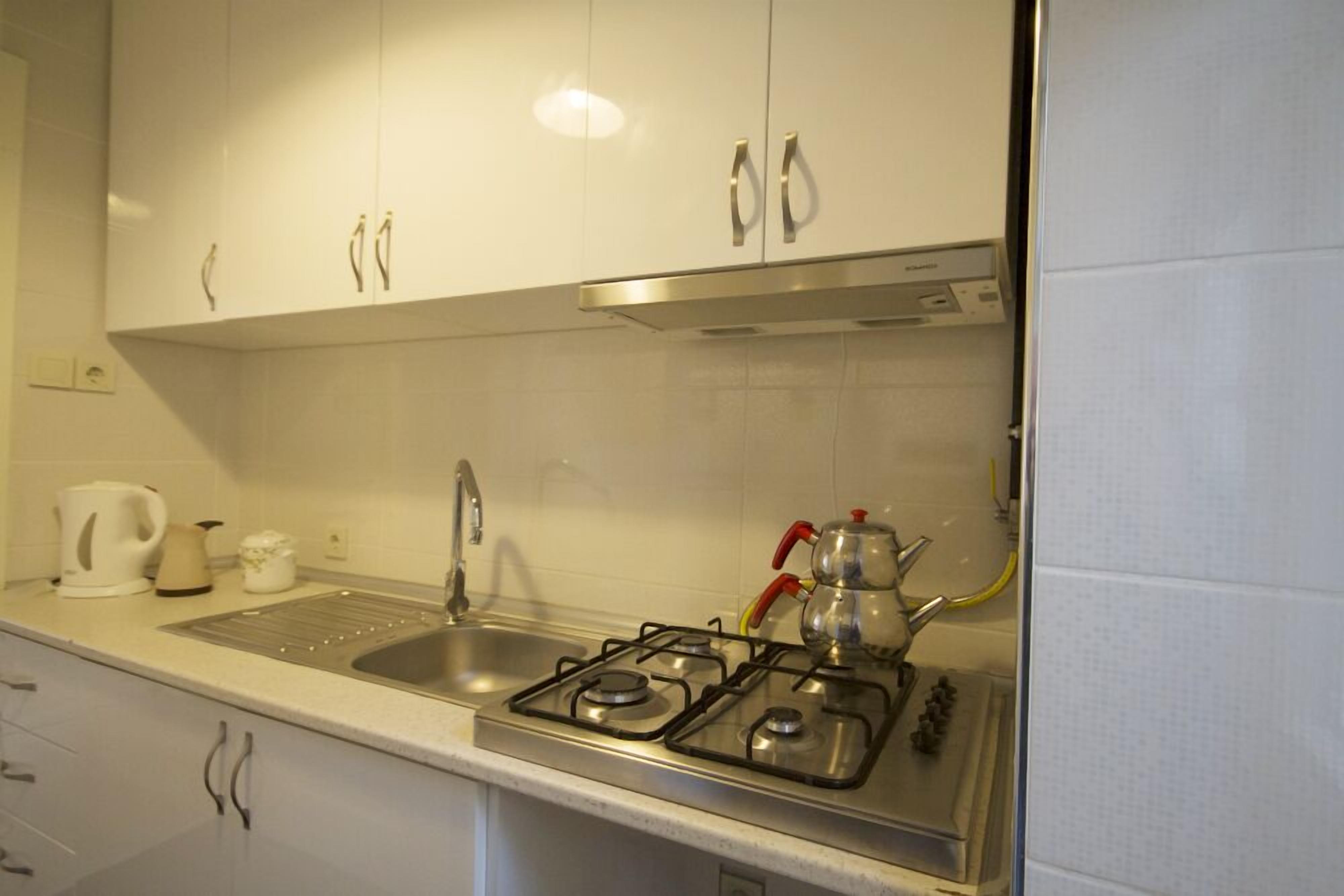 A kitchen with white cabinets, a gas stove, a sink, and a kettle.