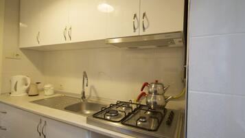 A kitchen with white cabinets, a gas stove, a sink, and a kettle.