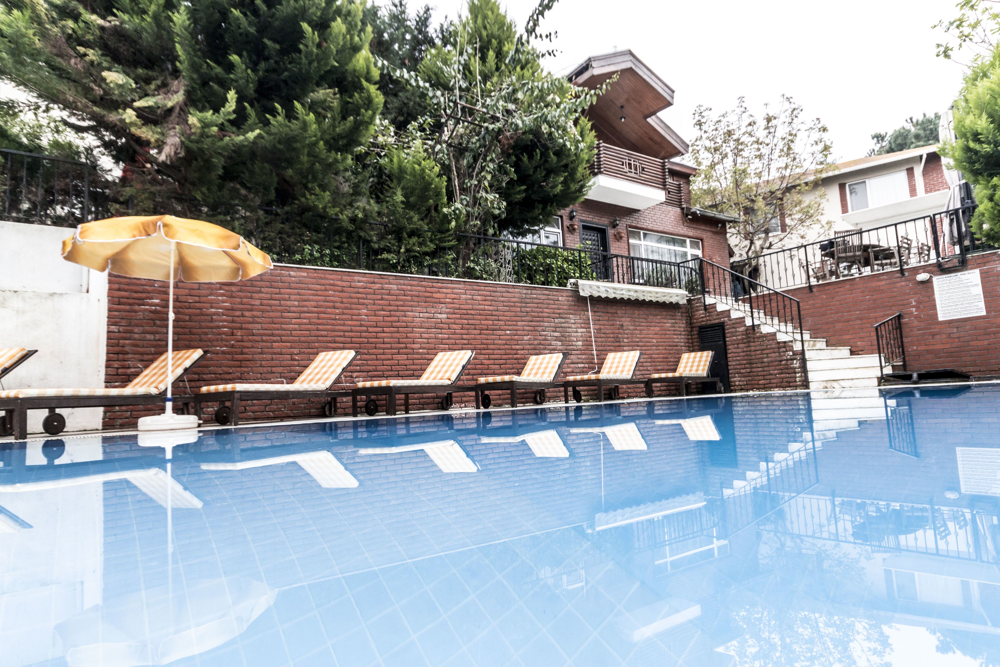 Piscina con sillas de descanso y una sombrilla, rodeada de muros de ladrillo y árboles.