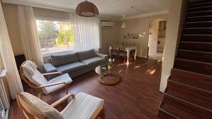 A modern living room with a sofa, two lounge chairs, a dining table, and a staircase. - Büyükada Apart Hotel - Karadağ Apart (Adalar)