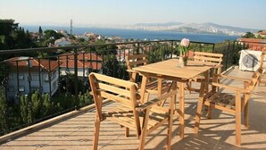 A wooden outdoor seating area with a table and benches, overlooking a cityscape and the sea. - Büyükada Apart Hotel - Karadağ Apart (Adalar)