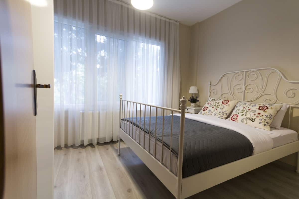 A bedroom with a bed, curtains, a nightstand, and a lamp.