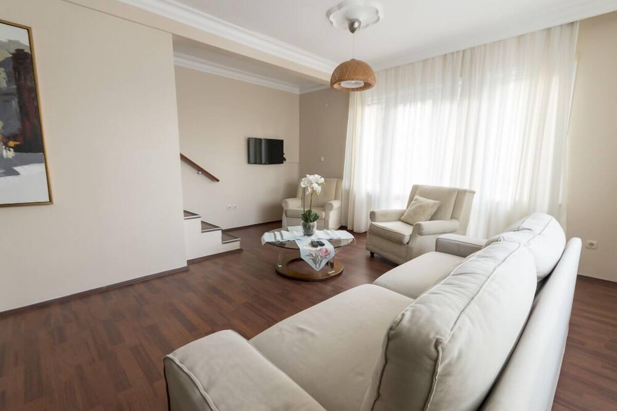 A modern living room with a beige sofa, a coffee table with a vase, a chair, and a staircase.