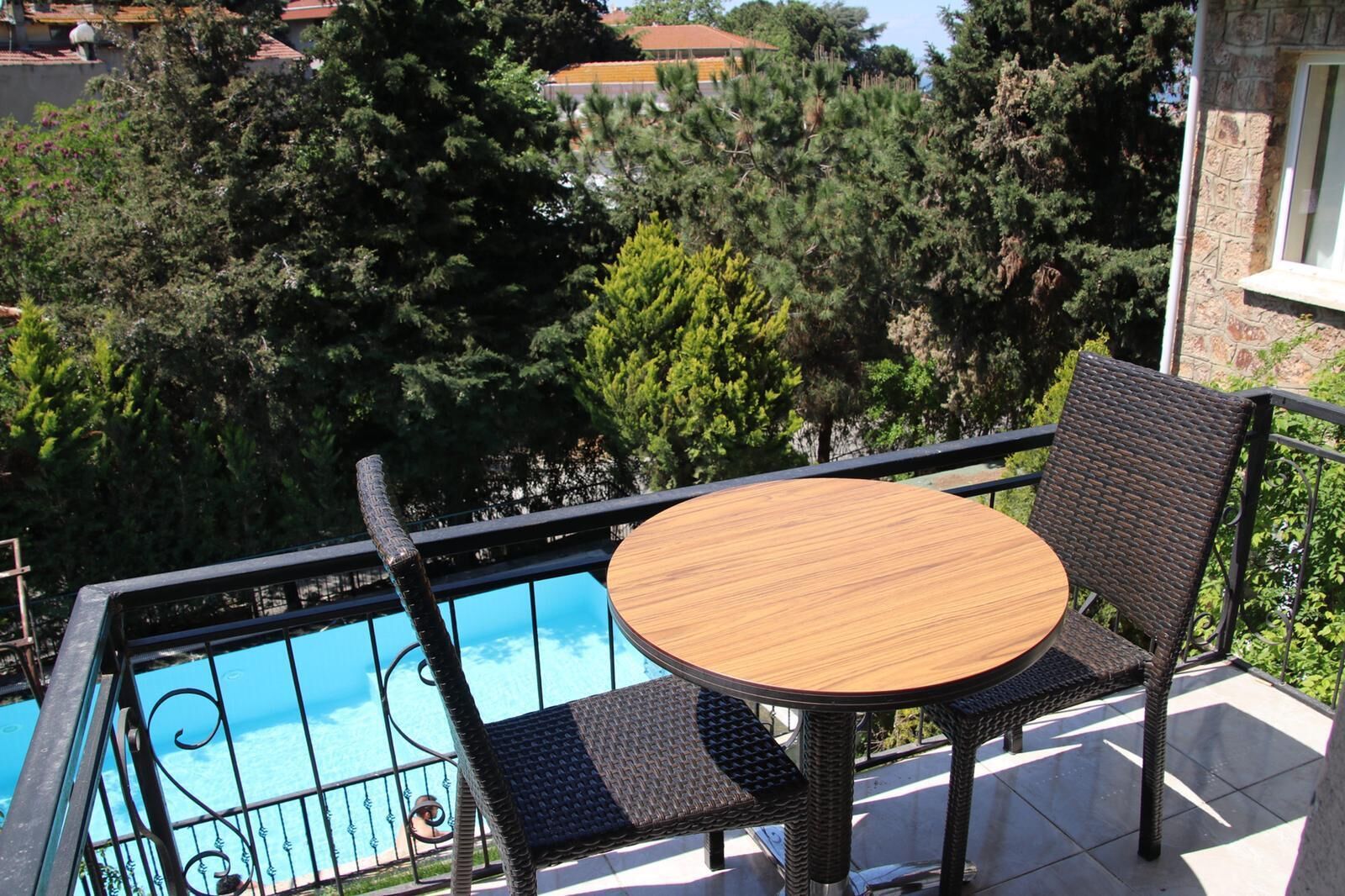 Un balcón con una mesa redonda y sillas de mimbre con vista a una piscina.