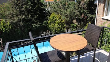 Un balcón con una mesa redonda y sillas de mimbre con vista a una piscina.