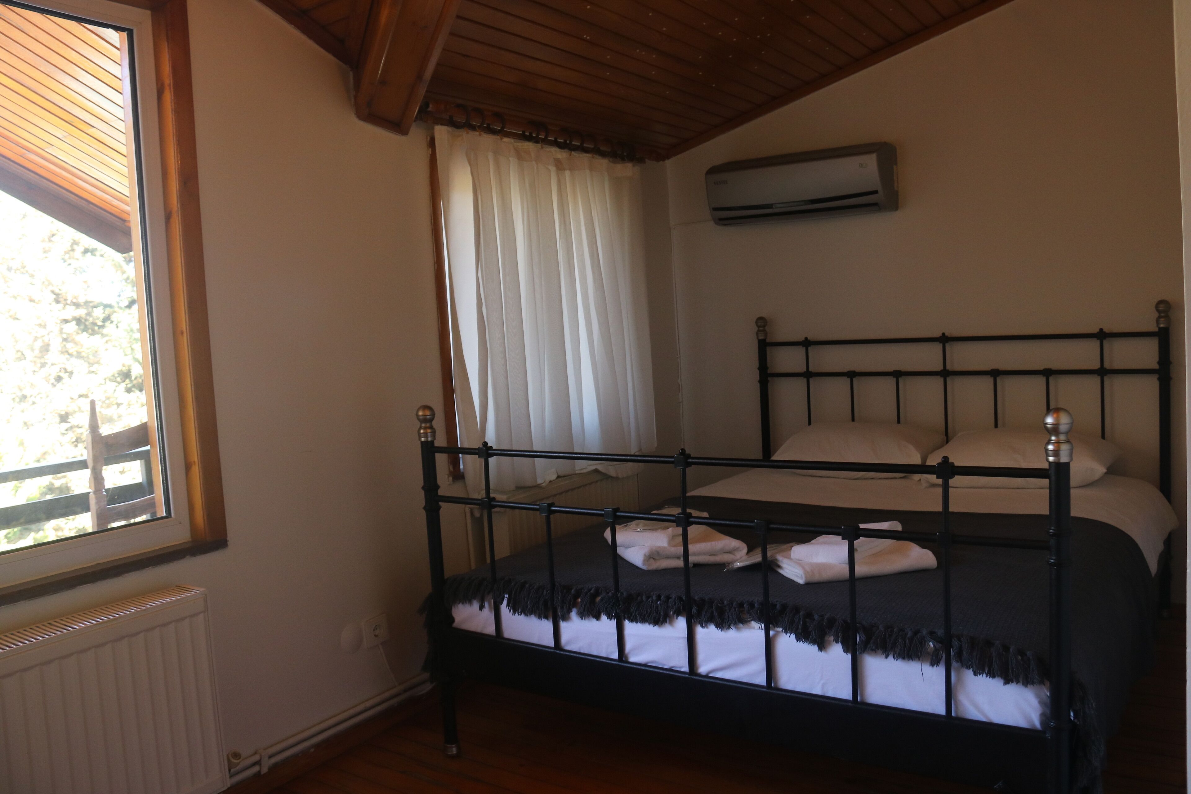 A bedroom with a bed, a window with blinds, an air conditioning unit, and a radiator.