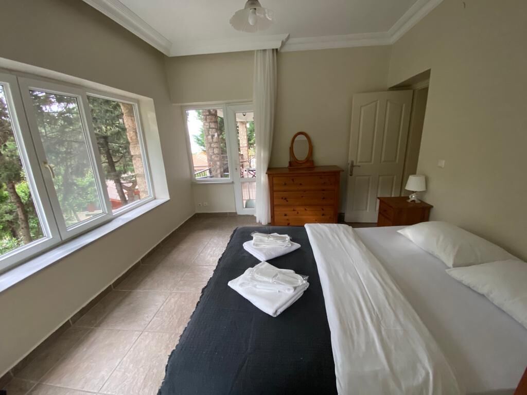 A bedroom with a bed, a dresser, a mirror, and a window with a view of trees.